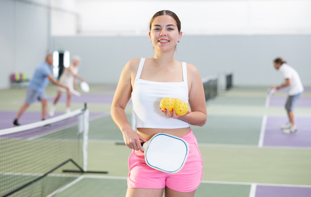 Positive girl looking at camera while playing pickleball at court indoor